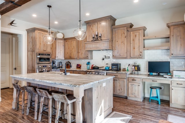 kitchen featuring decorative backsplash, an island with sink, light stone counters, double oven, and pendant lighting