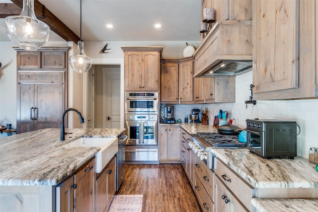 kitchen featuring custom range hood, hanging light fixtures, appliances with stainless steel finishes, a sink, and light stone countertops