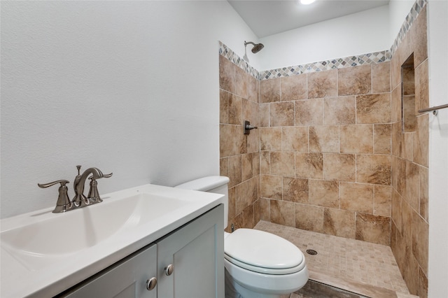 bathroom with tiled shower, vanity, and toilet