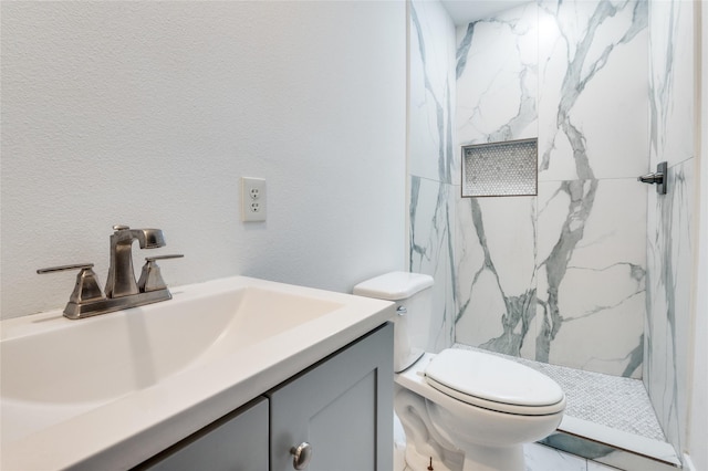 bathroom featuring a marble finish shower, a textured wall, vanity, and toilet