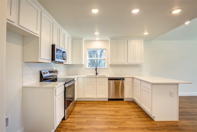 kitchen with a peninsula, stainless steel appliances, light countertops, white cabinetry, and a sink