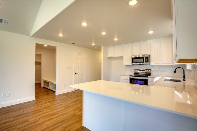 kitchen with a sink, a peninsula, stainless steel appliances, and light countertops