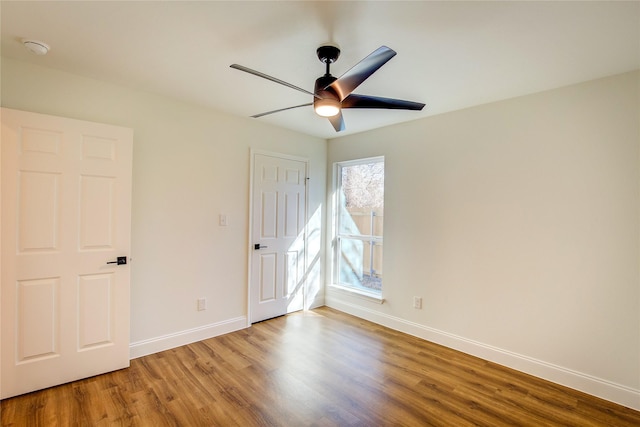 empty room with wood finished floors, a ceiling fan, and baseboards