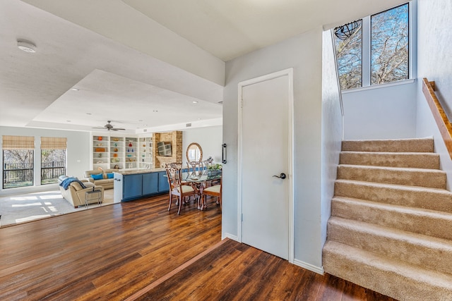 staircase featuring wood finished floors, a ceiling fan, and baseboards