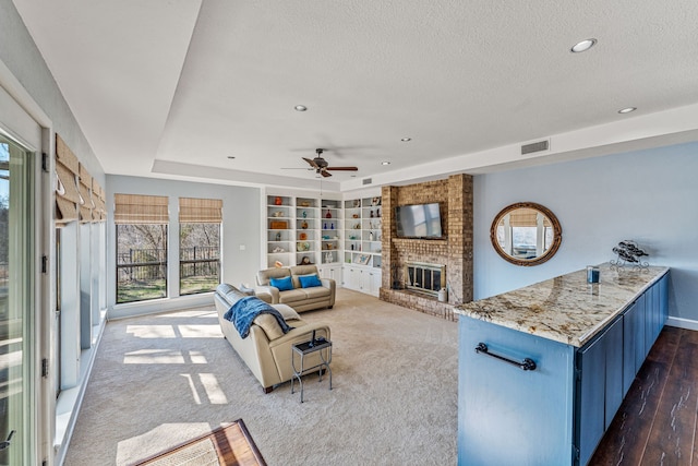 living room with visible vents, a ceiling fan, a tray ceiling, a textured ceiling, and a brick fireplace