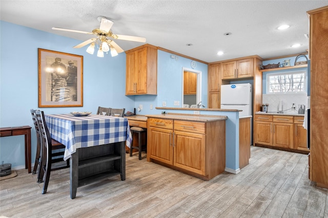 kitchen with light wood finished floors, a ceiling fan, freestanding refrigerator, a peninsula, and recessed lighting