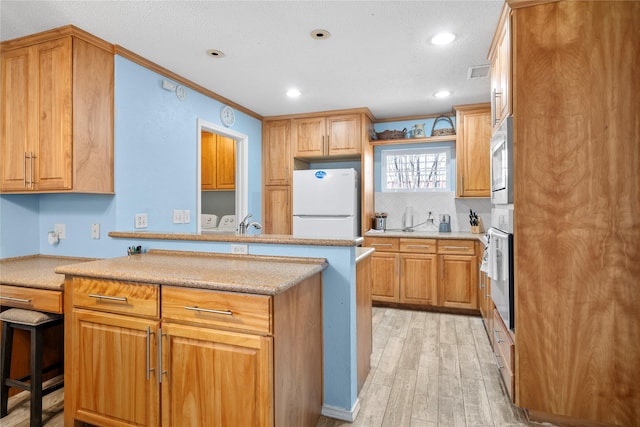 kitchen featuring white appliances, light wood finished floors, visible vents, ornamental molding, and a peninsula