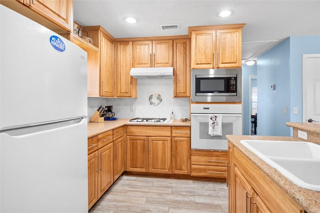 kitchen with light countertops, visible vents, decorative backsplash, white appliances, and under cabinet range hood