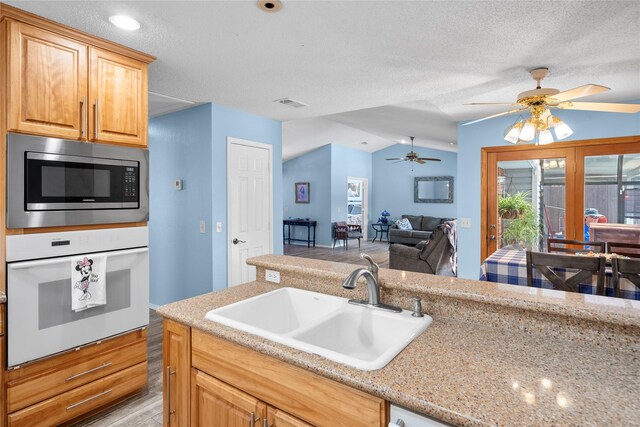 kitchen with oven, a sink, visible vents, vaulted ceiling, and stainless steel microwave