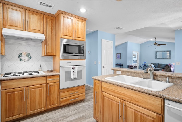 kitchen with light wood-style flooring, under cabinet range hood, white appliances, a sink, and visible vents