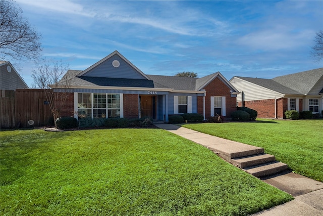 view of front facade featuring a shingled roof, a front yard, brick siding, and fence