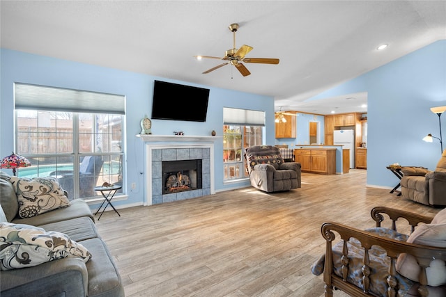 living room with light wood-style floors, a fireplace, plenty of natural light, and a ceiling fan