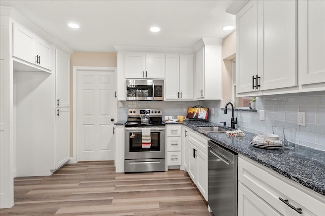 kitchen with light wood-style flooring, a sink, white cabinets, appliances with stainless steel finishes, and decorative backsplash