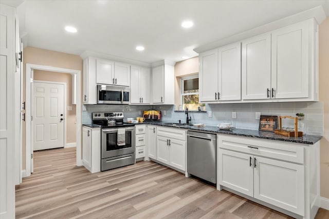 kitchen with white cabinets, light wood-style flooring, a sink, stainless steel appliances, and backsplash