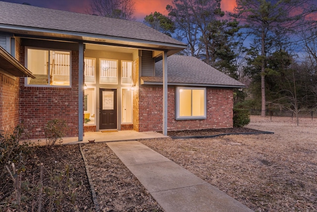 entrance to property with brick siding, a shingled roof, and fence