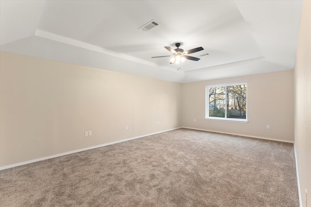 empty room featuring a tray ceiling, carpet, visible vents, ceiling fan, and baseboards