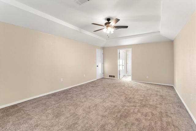 carpeted spare room featuring ceiling fan, a tray ceiling, visible vents, and baseboards