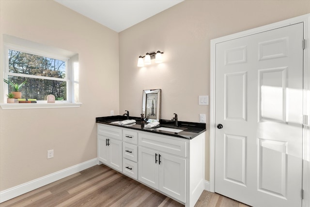 full bath with double vanity, baseboards, a sink, and wood finished floors