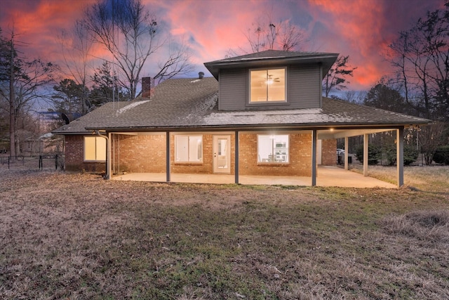 rear view of house with brick siding, a chimney, a lawn, and a patio