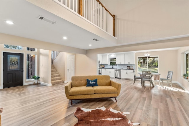 living area with light wood-style floors, visible vents, baseboards, and stairs