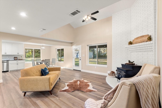 living room featuring light wood-style floors, a wood stove, visible vents, and baseboards