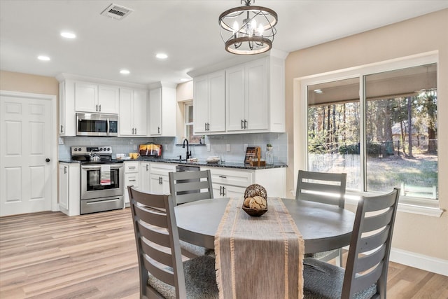 kitchen with visible vents, white cabinets, appliances with stainless steel finishes, light wood-type flooring, and pendant lighting