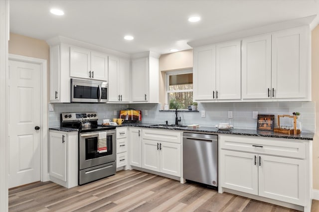 kitchen featuring light wood-style flooring, dark stone countertops, stainless steel appliances, white cabinetry, and a sink