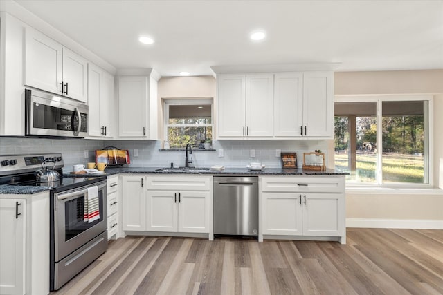 kitchen featuring white cabinets, dark stone countertops, stainless steel appliances, and a sink