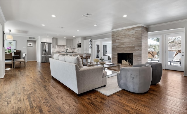 living area with dark wood finished floors, crown molding, and a tiled fireplace