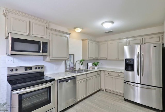 kitchen featuring light stone counters, stainless steel appliances, wood finish floors, a sink, and visible vents