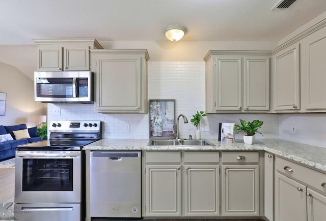 kitchen featuring visible vents, decorative backsplash, light stone counters, appliances with stainless steel finishes, and a sink