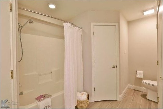 full bathroom with shower / tub combo, baseboards, and toilet