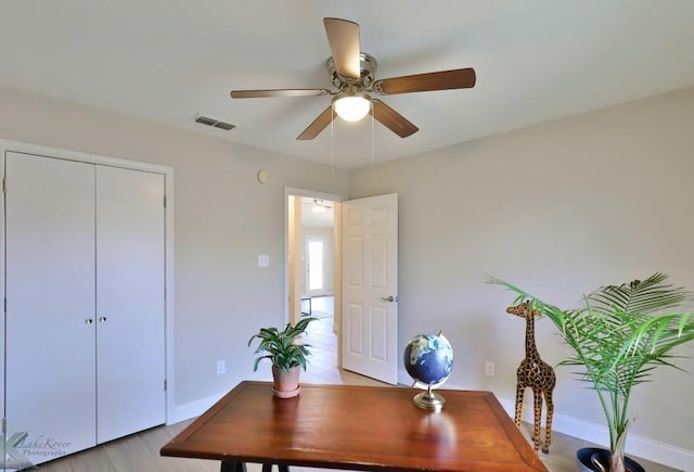 office featuring light wood-style floors, a ceiling fan, visible vents, and baseboards