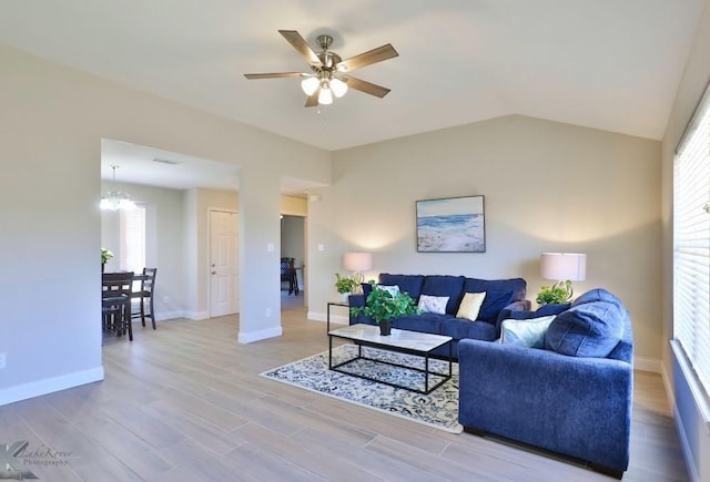 living room featuring vaulted ceiling, ceiling fan with notable chandelier, wood finished floors, and baseboards