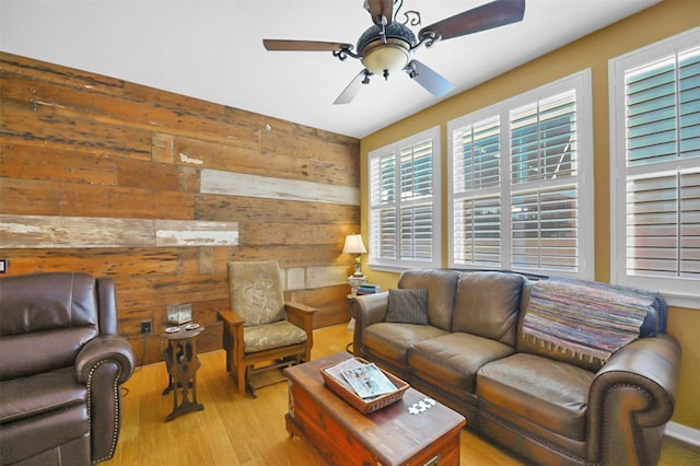 living room with a ceiling fan, wood walls, and light wood finished floors