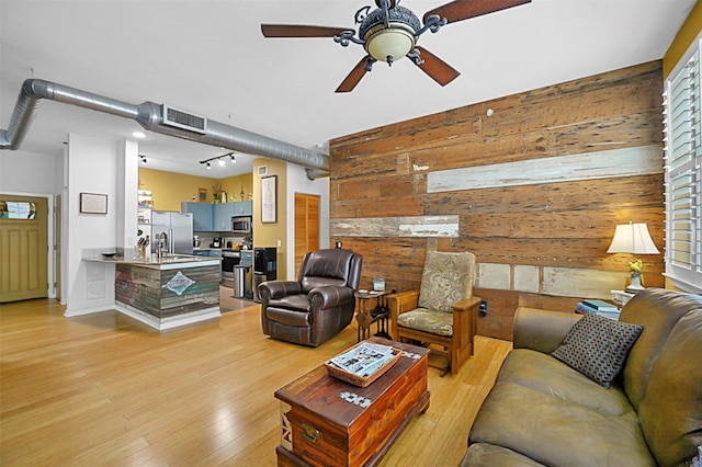 living room featuring visible vents, rail lighting, a ceiling fan, wood walls, and light wood-type flooring