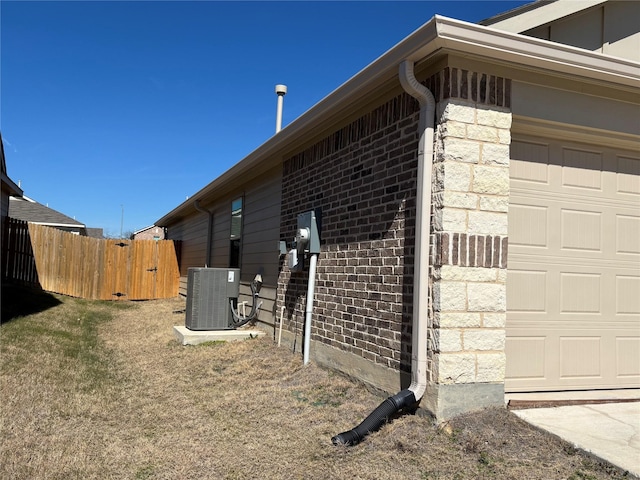 view of side of home featuring stone siding, an attached garage, fence, central AC, and brick siding