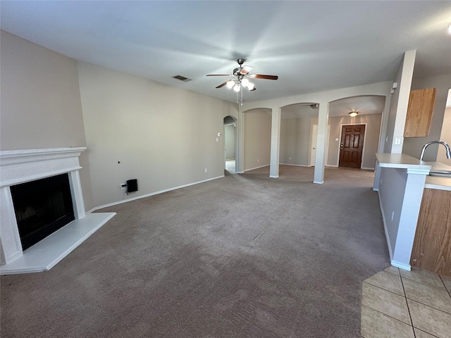 unfurnished living room with arched walkways, a fireplace with raised hearth, visible vents, carpet flooring, and ceiling fan