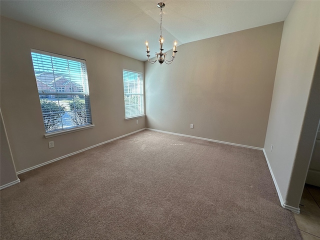 carpeted empty room with vaulted ceiling, a notable chandelier, and baseboards