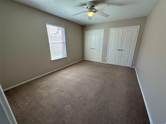 unfurnished bedroom featuring dark colored carpet, two closets, a ceiling fan, and baseboards