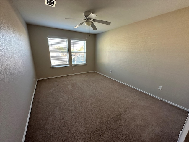 unfurnished room with a ceiling fan, visible vents, dark carpet, and baseboards