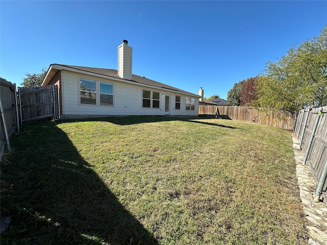 rear view of house with a fenced backyard, a yard, and a chimney