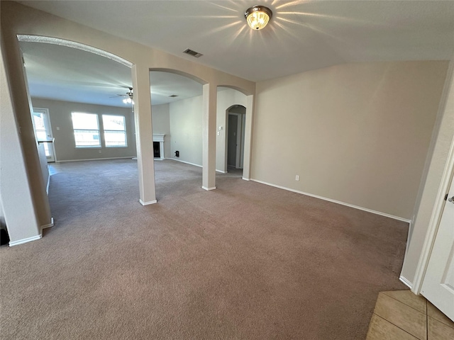 carpeted empty room featuring arched walkways, a fireplace, visible vents, ceiling fan, and baseboards