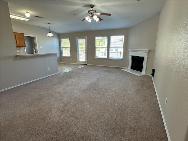 unfurnished living room with light carpet, baseboards, visible vents, a fireplace with raised hearth, and ceiling fan