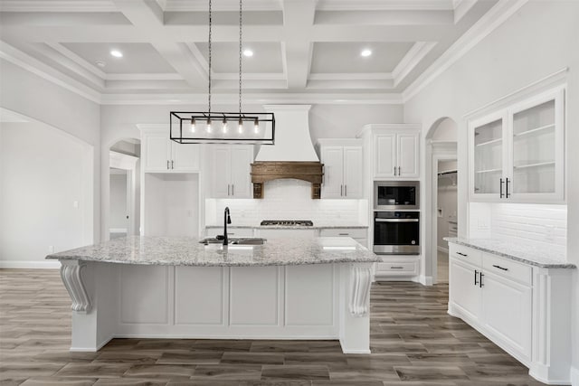 kitchen with arched walkways, stainless steel appliances, a sink, white cabinetry, and custom exhaust hood