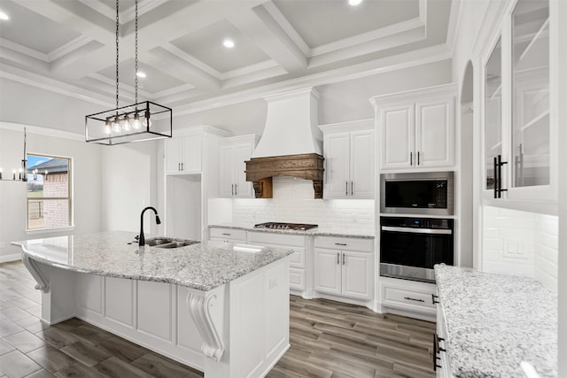 kitchen featuring backsplash, appliances with stainless steel finishes, white cabinets, a sink, and premium range hood