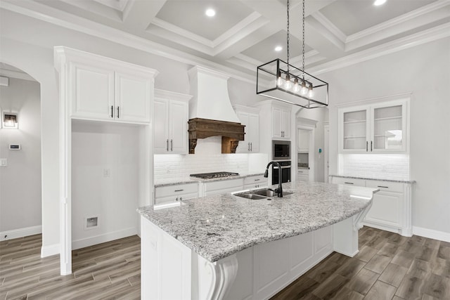 kitchen featuring arched walkways, white cabinets, custom exhaust hood, stainless steel appliances, and a sink