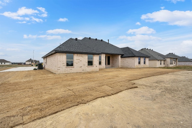 view of front of home with roof with shingles, central AC unit, and brick siding