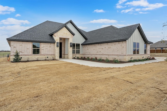 view of front of house with a shingled roof, brick siding, fence, board and batten siding, and a front yard