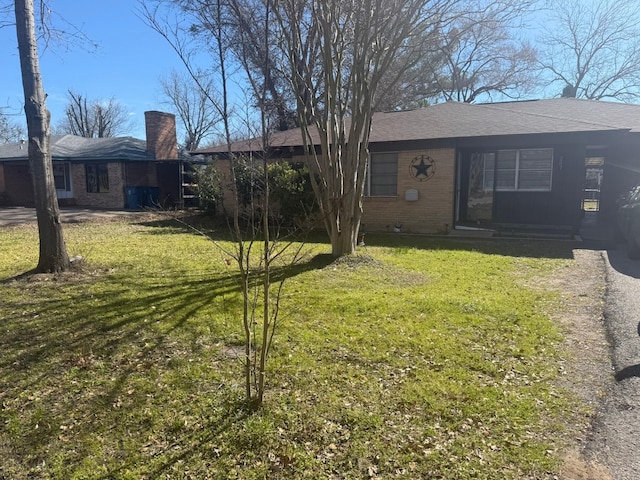 view of front facade featuring brick siding, a front lawn, and a chimney